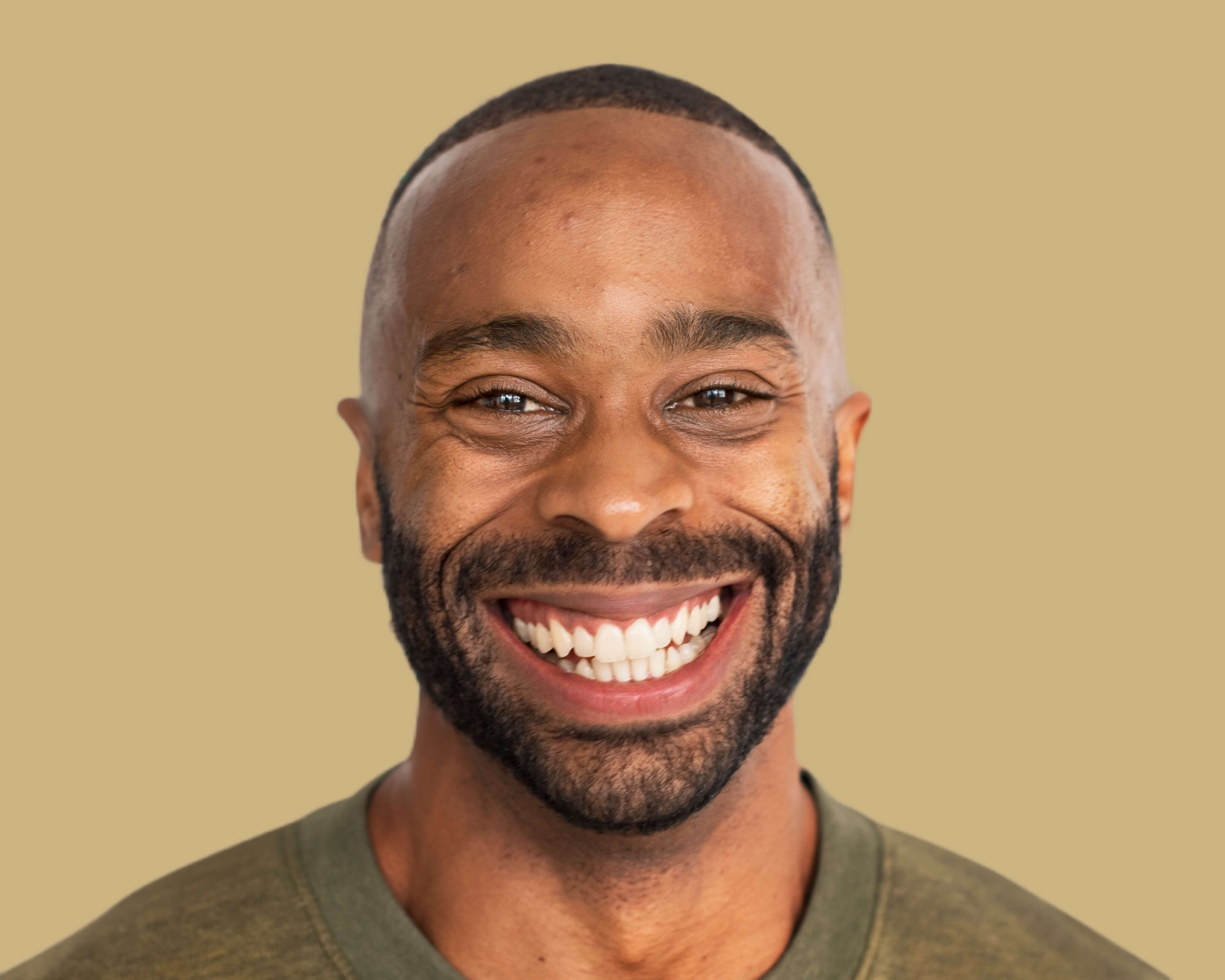 A close up of a man with a big smile, with a very short hair and a very well trimmed beard. Showcasing his wrinkle free forehead.